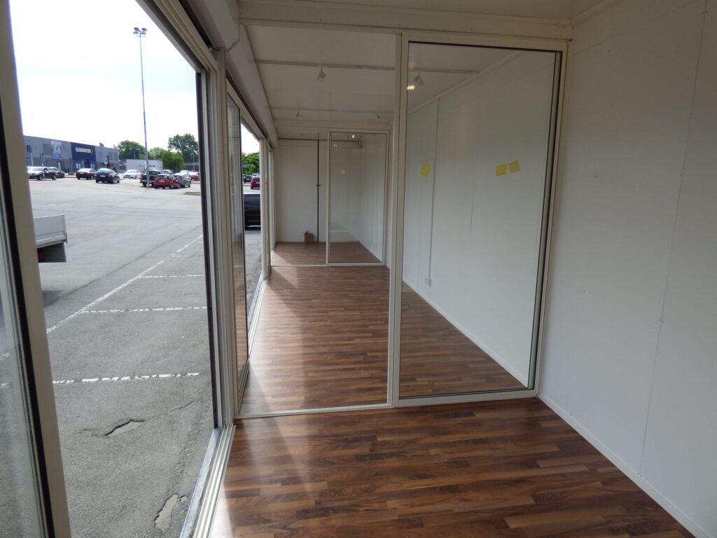 Interiör i butikscontainer med glasväggar mot parkeringsplats och avdelare mellan rum, byggd av LCS