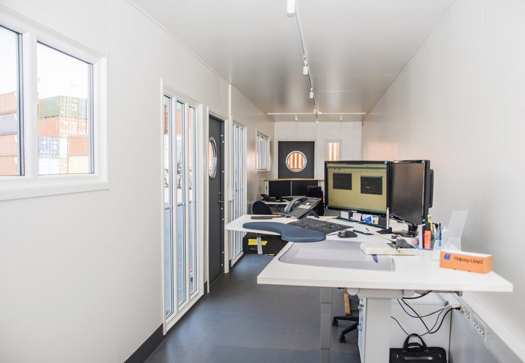 Langsgaende vy over kontorsyta med tva arbetsplatser och sparbelysning i receptionscontainer byggd av LCS