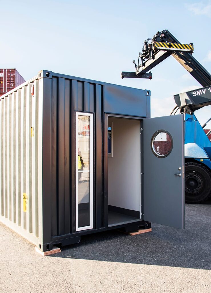 Kortsida på receptionscontainer med öppnad gångdörr och runt fönster, byggd av LCS på containerterminal