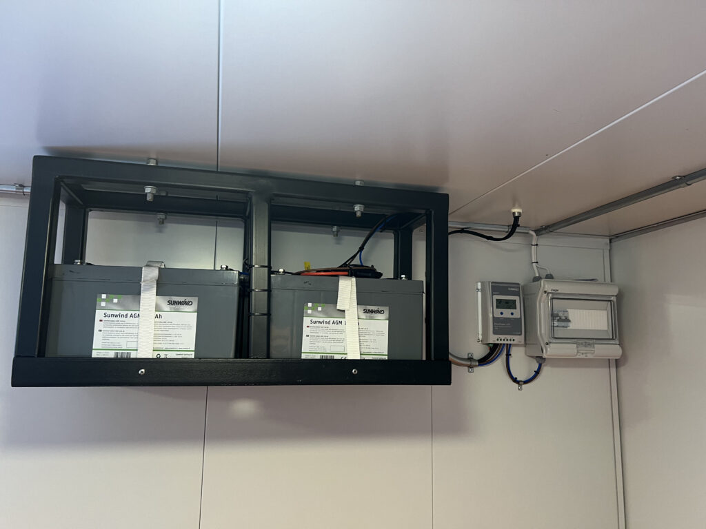 Närbild på batterier och laddregulator monterade i tak i miljörumscontainer med solcellsdrift, byggd av LCS