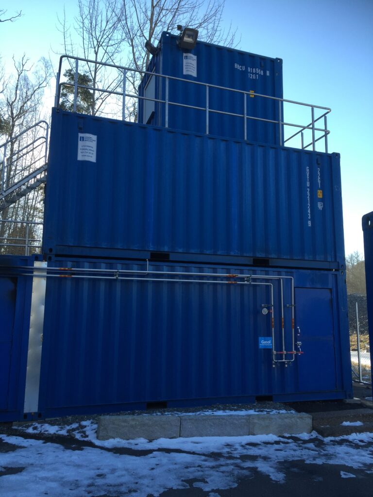 Staplade blå containrar med rörledningar och räcken i övningsmodul för brandövning, byggd av LCS