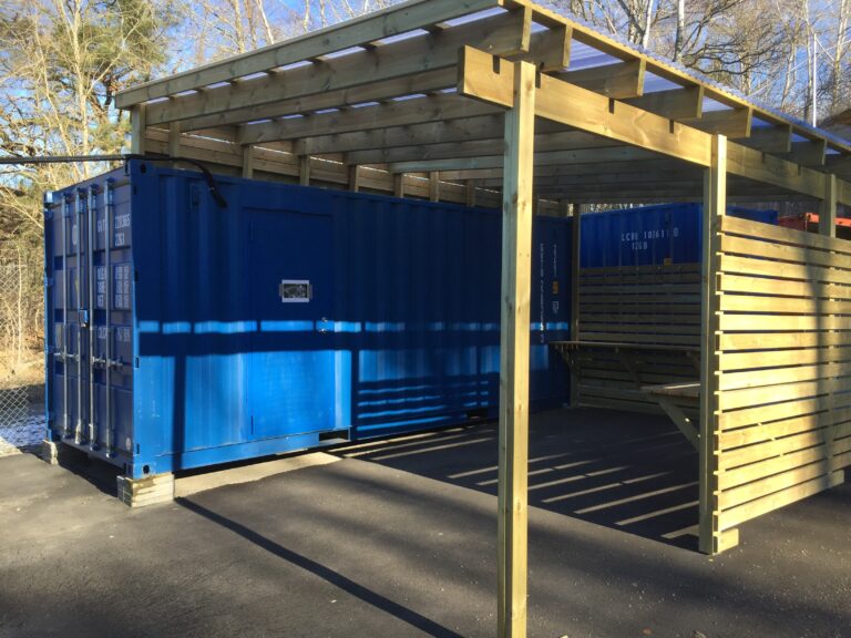 Träöverbyggnad med tak och blå containrar i övningsmodul för brandövning, byggd av LCS