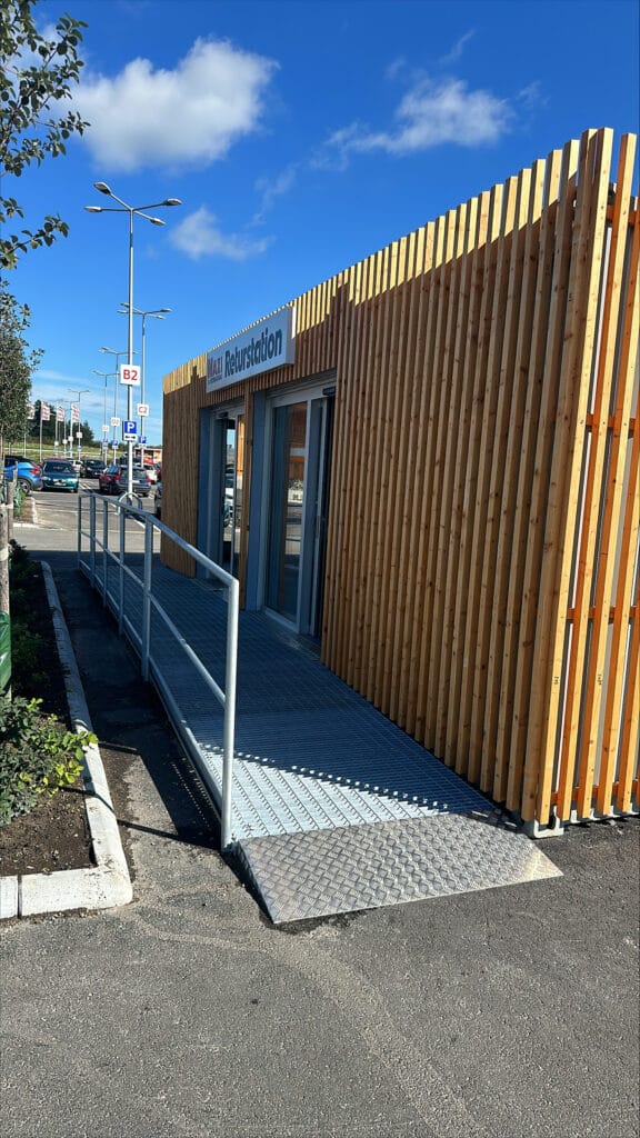 Exteriör entré med träfasad, ramp och glasdörrar på pantstationscontainer byggd av LCS