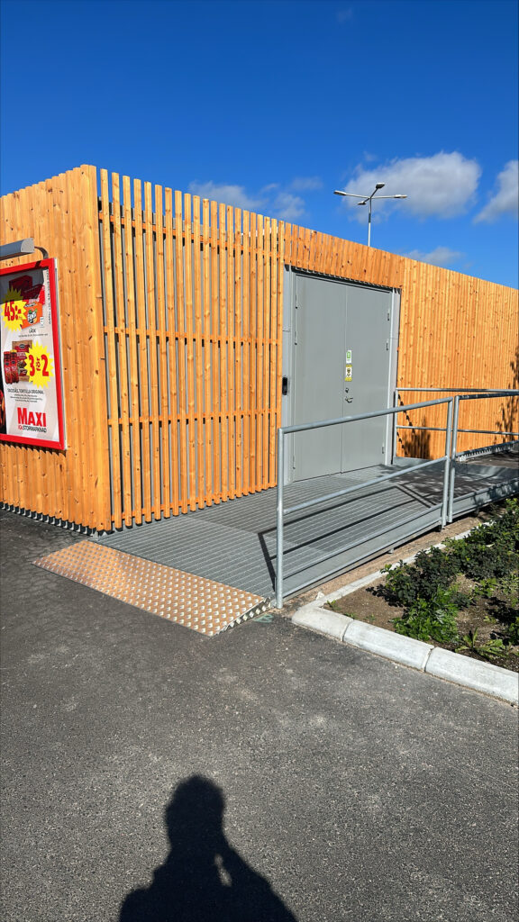 Kortsida på pantstationscontainer med träfasad, dubbeldörr och ramp till maskindelen, byggd av LCS