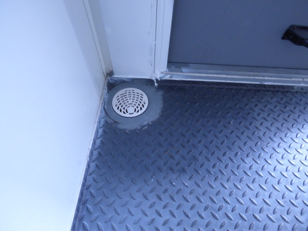 Närbild på golvbrunn i riffelmönstrat stålgolv i reservkraftscontainer för fartyg, byggd av LCS