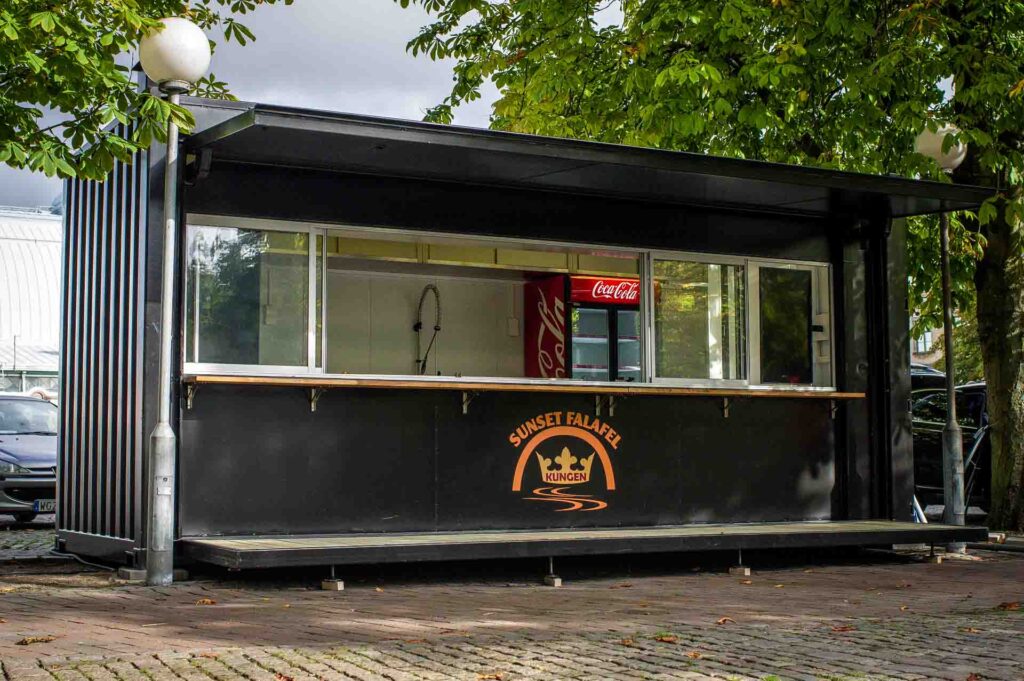 Framsida på serveringscontainer med utfällt golv och glasparti mot kunder på torg, byggd av LCS