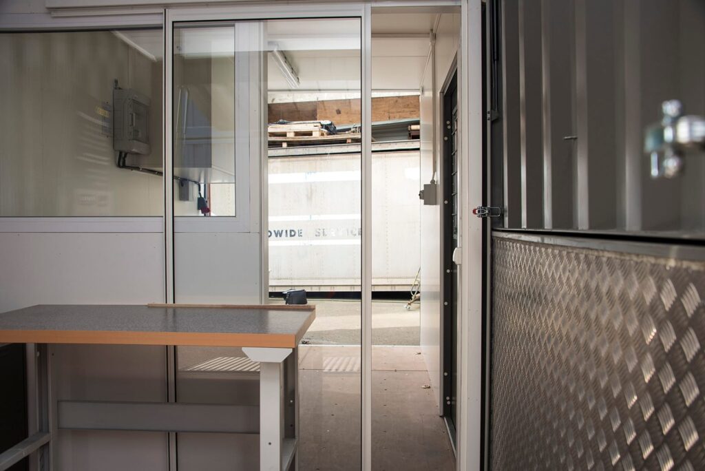 Glasad skjutdörr mellan övningsrum och observationsrum i utbildningscontainer byggd av LCS