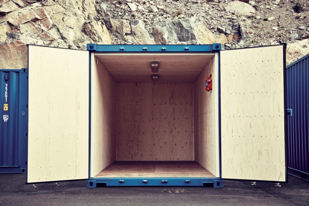 Öppen, isolerad lagercontainer med plywoodklädda väggar, belysning i taket och båda dörrarna uppslagna utomhus.